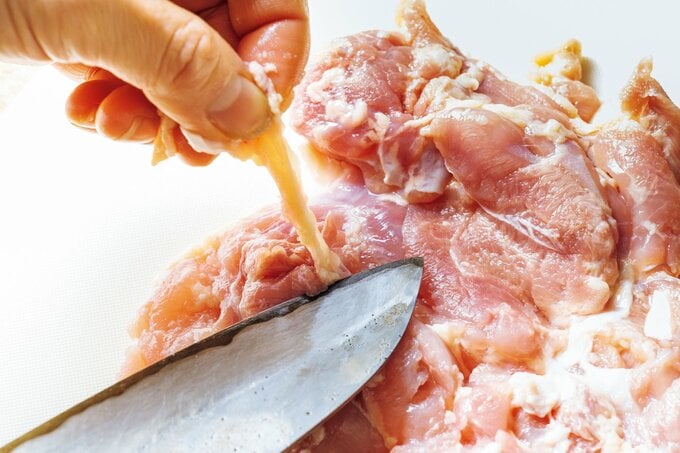 鶏もも肉の皮を包丁で削いでいる手もと