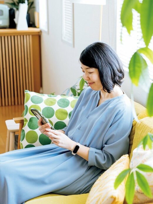 水色のワンピースを着た女性がソファーでスマホを見る様子