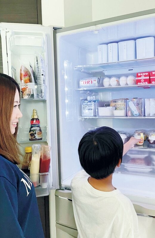 ドアがあいた冷蔵庫の前に立つ女性と男児