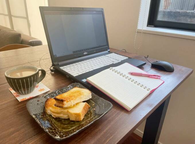 パソコンの上に手帳、隣にパンとコップ