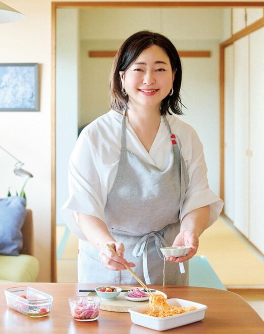 白いトップスにグレーのエプロンをかけた女性がお皿に料理を盛る様子