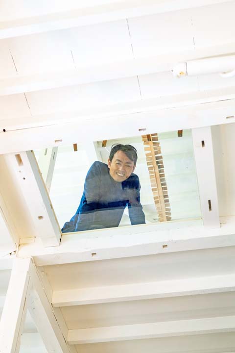 ガラス床越しに2階から1階を見る田中さん