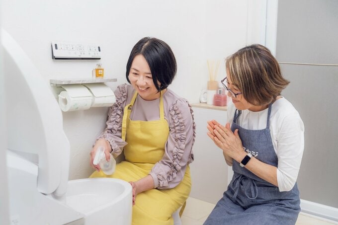 便器にスプレーをかける女性と見守る女性