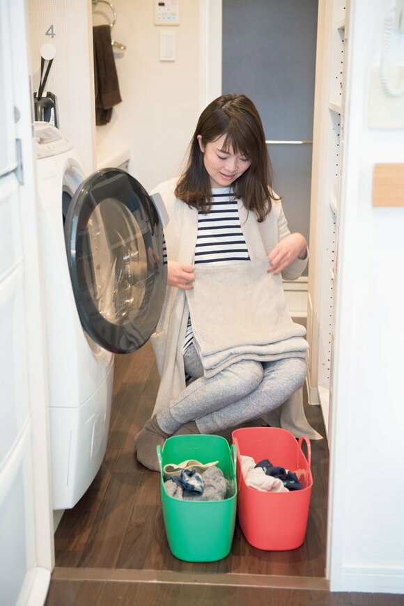 洗濯機の前で洗濯物を畳む女性