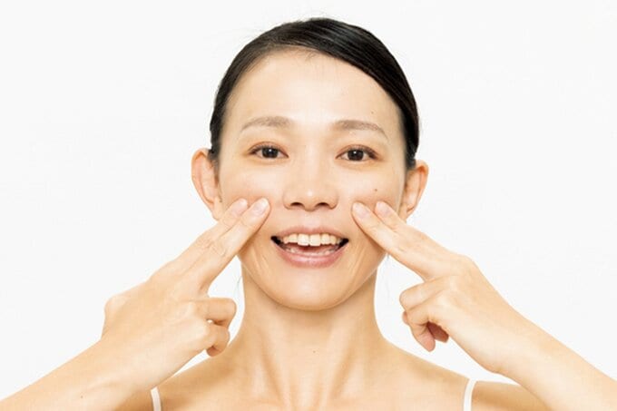 両頬に人差し指と中指をあてる女性