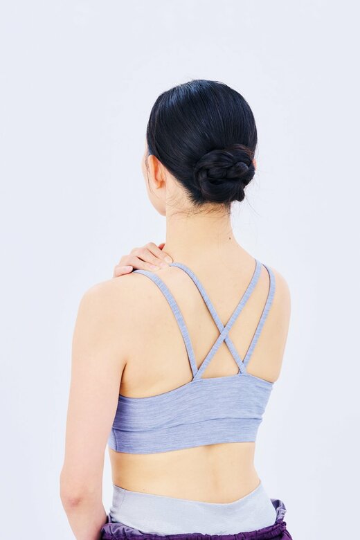 首の付け根を指で押す女性の後ろ姿