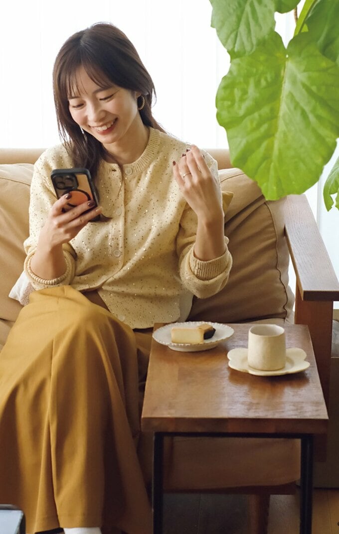 ソファに座りスマホを操作する女性と、サイドテーブルのケーキとコーヒーカップ