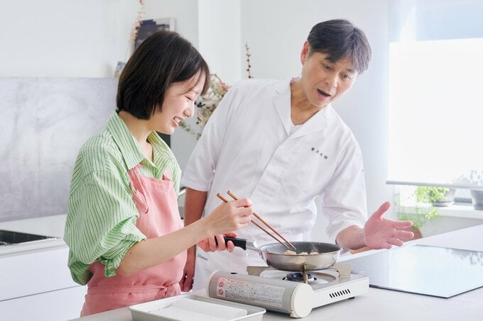 キッチンで料理する女性とのぞき込む男性