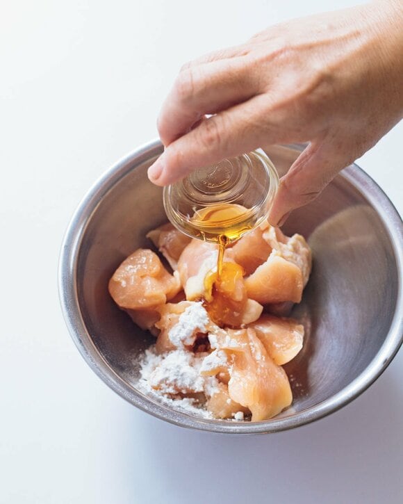 ボウルに入った鶏肉にゴマ油を入れる様子