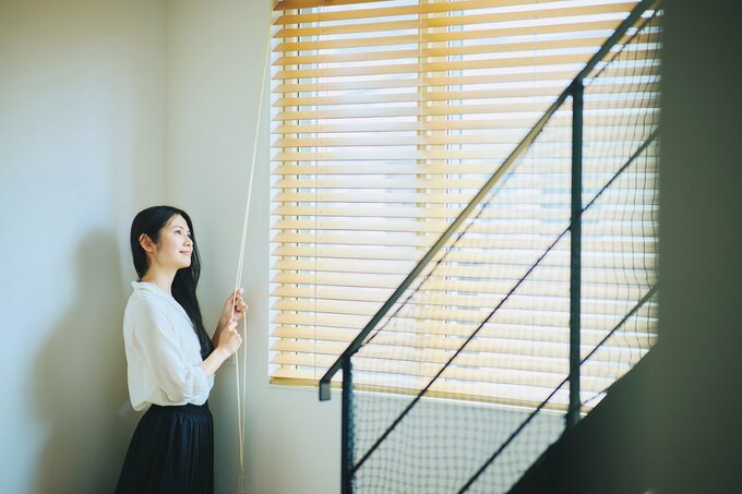 ブラインドを調整して日光を取り入れる女性