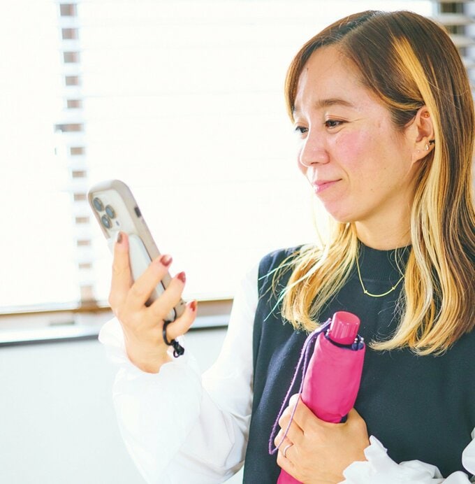 外出前にスマートフォンで天気予報を確認する女性