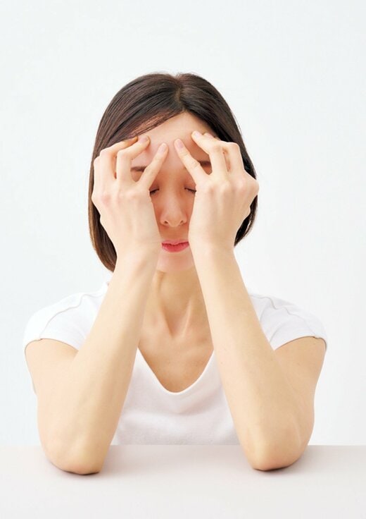 テーブルに肘をついておでこを指で押し上げる女性