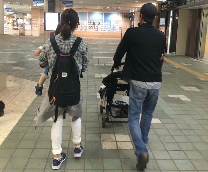 2人の後ろ姿。右側にベビーカーを押す男性、左側に子どもを抱っこする女性。