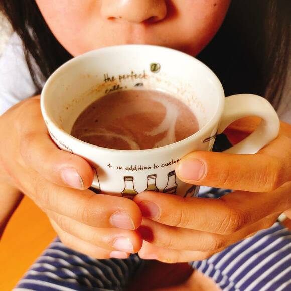 ホットチョコレートが入ったマグカップを両手で持つ