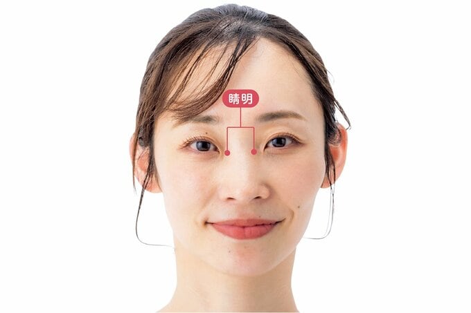 正面を見て微笑む女性の鼻のつけ根のツボ「睛明」