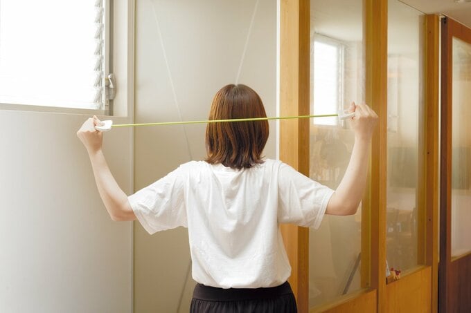 トレーニング用チューブを背面で引っ張る女性の後ろ姿