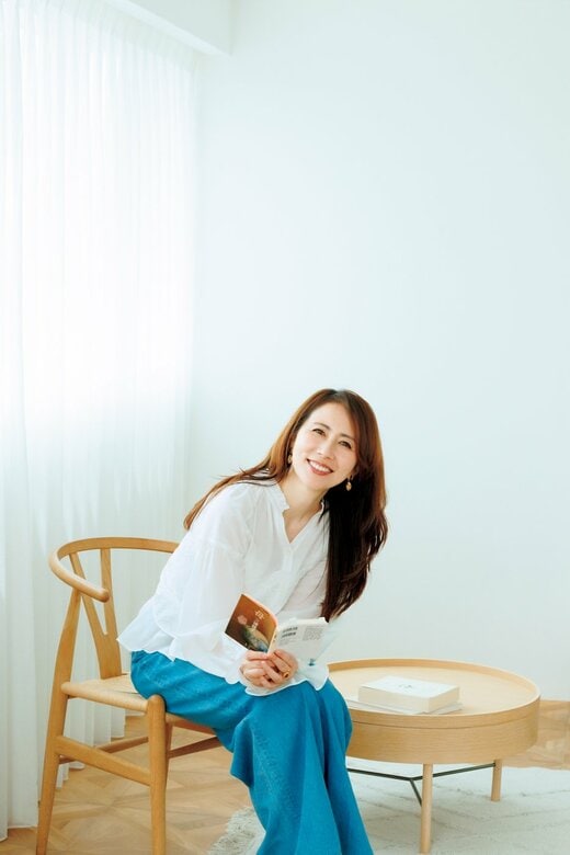 椅子に座って本を持っている白のブラウスにジーンズ姿の女性