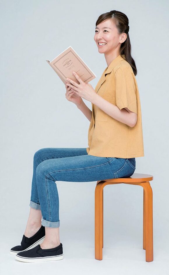 本をもつ女性右足かかとを少しあげる