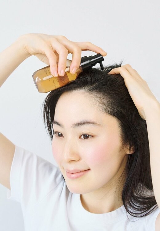 ボトルを手に持ち頭皮に頭皮用美容液をたらす女性