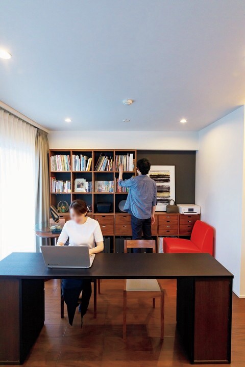 デスクで作業する妻と本を探す夫