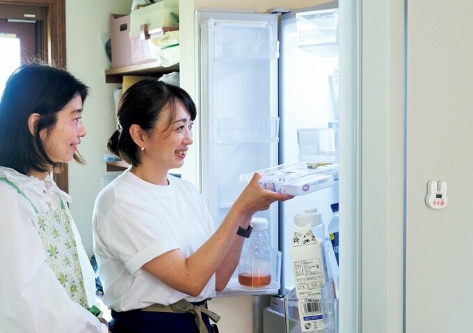 食品を冷蔵庫に入れる女性とその様子を見る女性