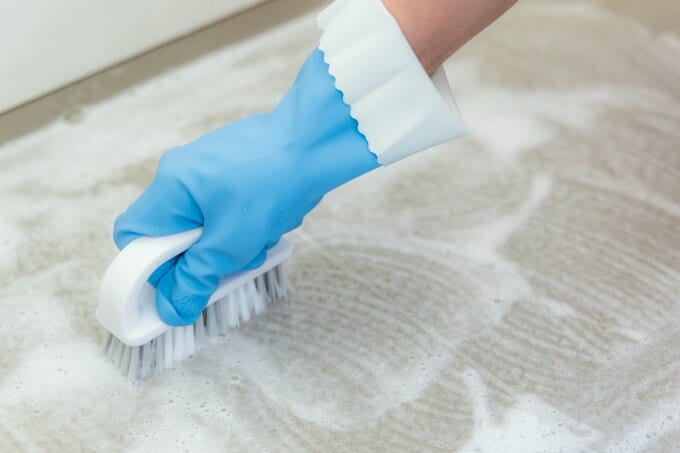 床のぬめりや赤カビをブラシでこすり落とす手元