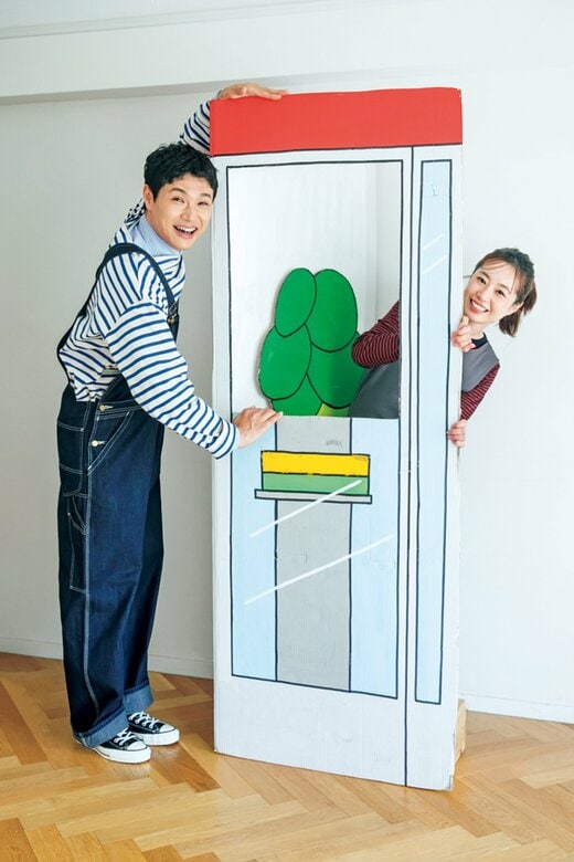 段ボール作品に手を添える男性と、作品から顔をのぞかせる笑顔の女性