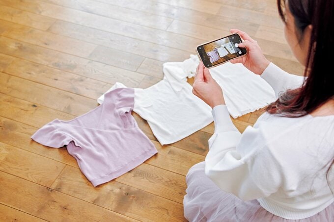床に並べた服をスマホで撮る様子