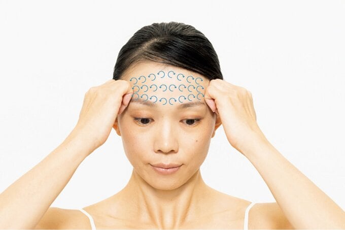 こめかみに向かってマッサージをする女性