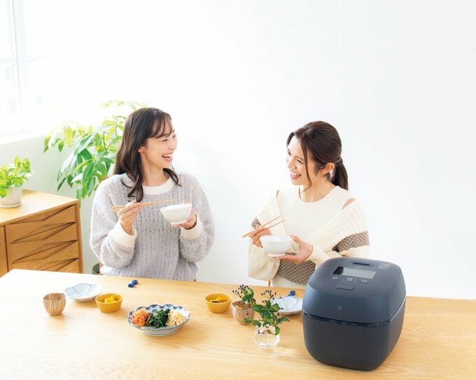 黒い炊飯器が置かれた食卓で食事をする2人の女性