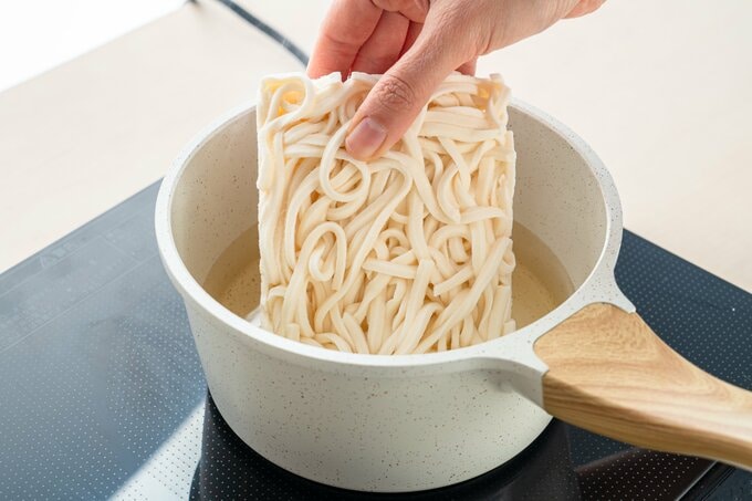 白だしを加えた鍋に冷凍うどんを入れている
