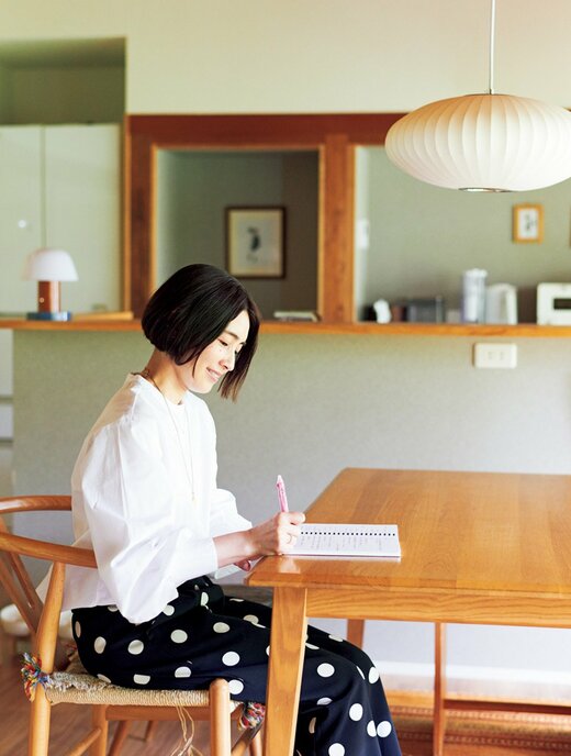 ダイニングテーブルにつきペンでノートに書きこんでいる女性