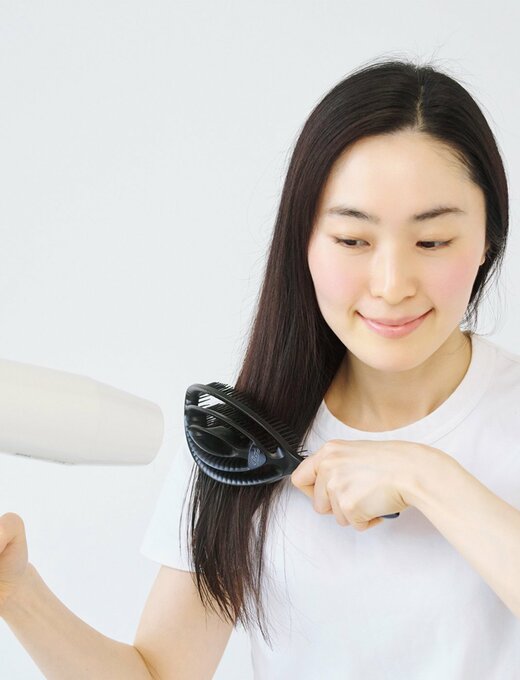 髪をブラシでとかしながらドライヤーで乾かしている女性