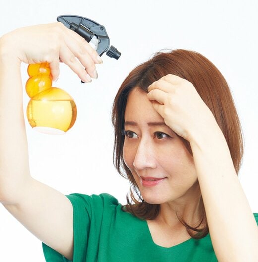 髪の根元部分をスプレーボトルの水で濡らす女性