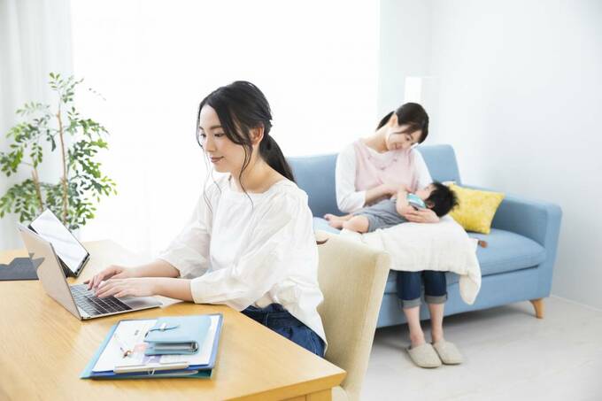 パソコンの前の女性の後ろに子どもを抱く女性