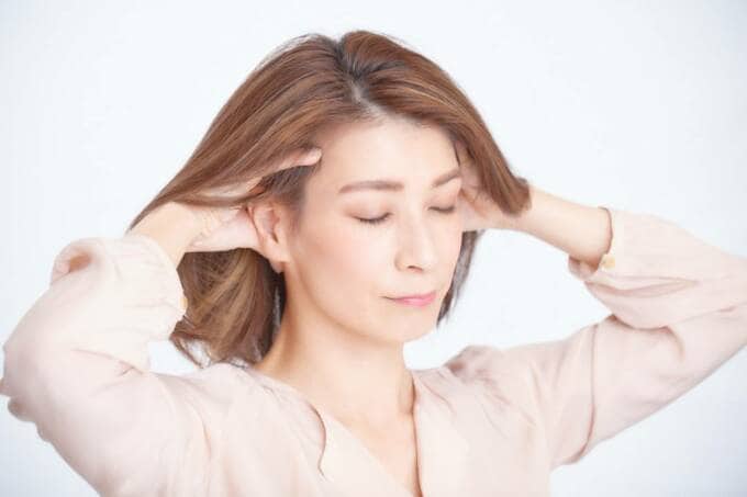 両手で耳のうしろをもむ女性
