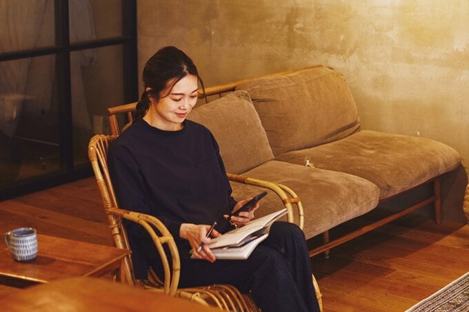 ソファに座って手帳とスマホを眺める女性