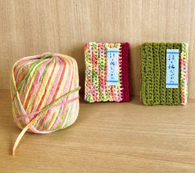 カラフルな色が混ざっている毛糸玉と手編みの豆本カバー
