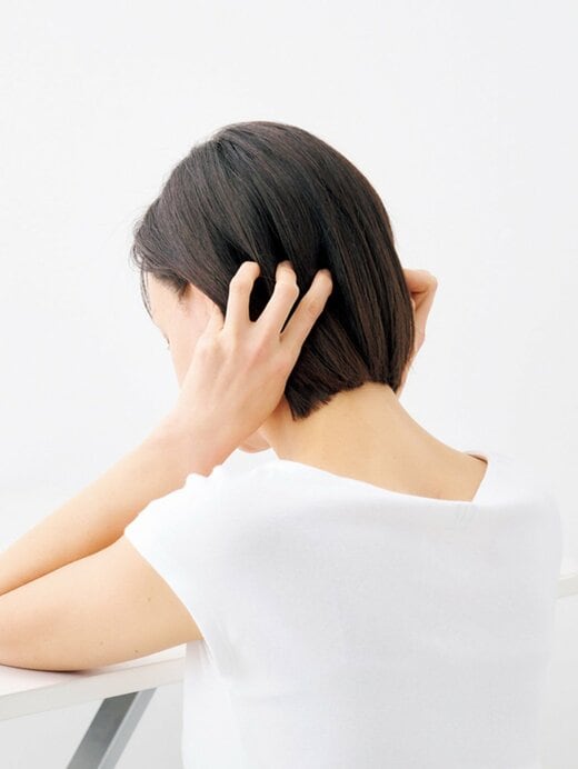 テーブルに肘をついて耳のつけ根を指で押し上げる女性の後ろ姿