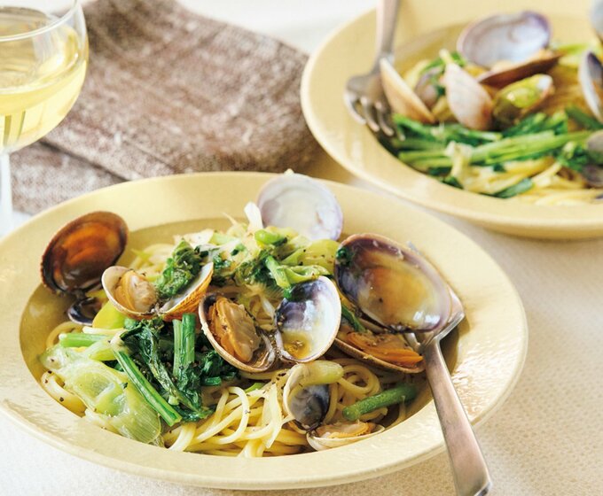 黄色い皿に盛られたアサリと香味野菜が入ったパスタと白のグラスワイン