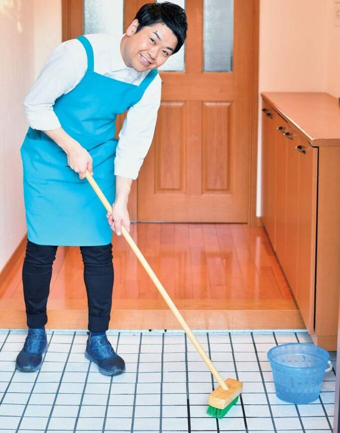 玄関をデッキブラシでこする男性