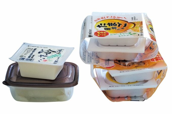 タッパーに入った豆腐の上に置かれた未使用の豆腐、2パックずつまとめられて重なっている納豆