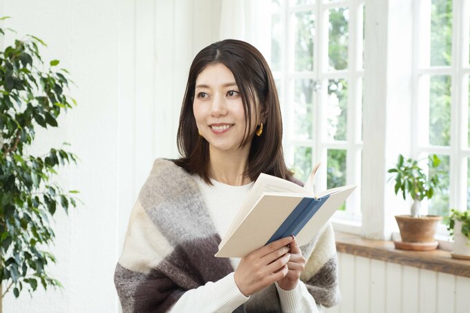女性がブランケットを肩にかけ、開いた本を持っている