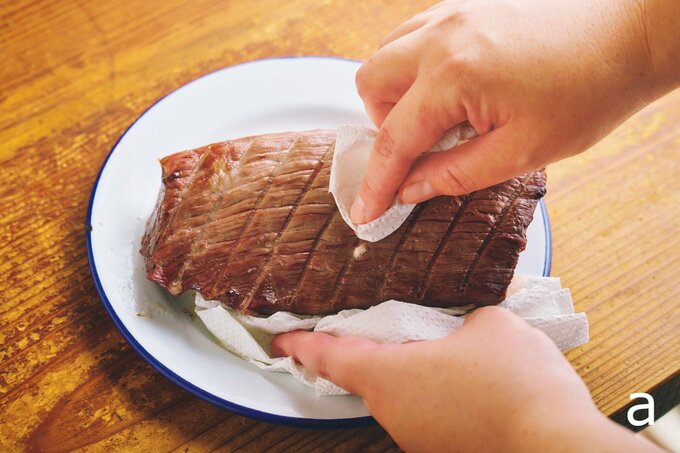 焼いた肉の表面についたアクをふく様子