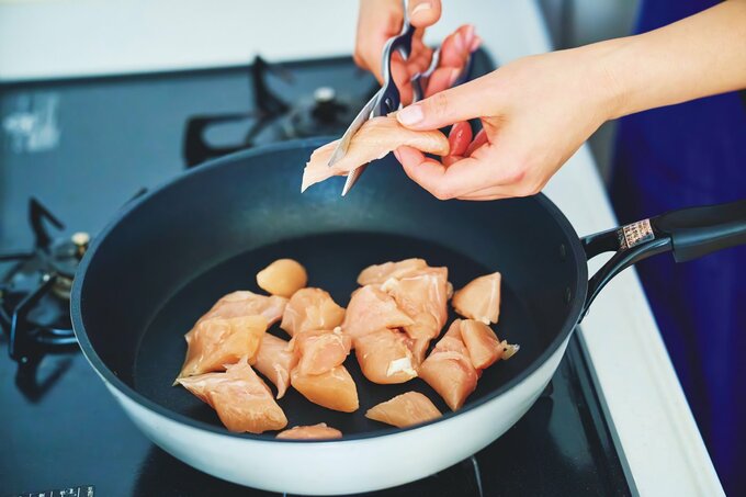フライパンのうえでキッチンバサミで鶏肉を切っている様子