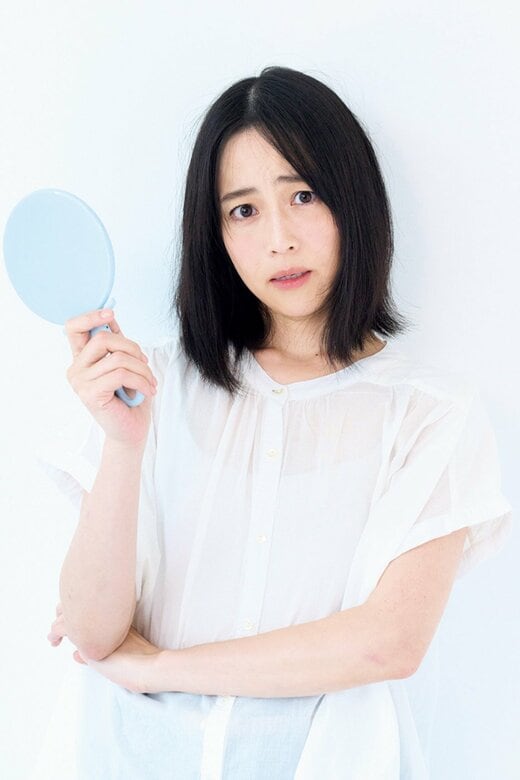 困った顔で手鏡を持つ女性