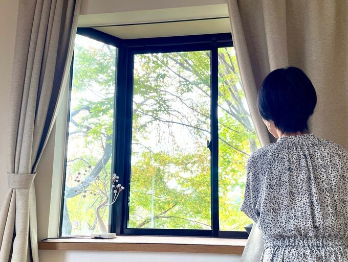 窓の外を眺めながらカーテンを開ける女性