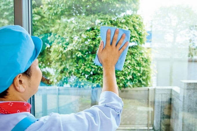 窓を磨いている青い帽子をかぶった男性の後ろ姿と手元