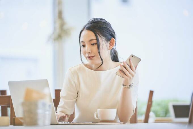 パソコンを操作しながらスマホを持つ女性