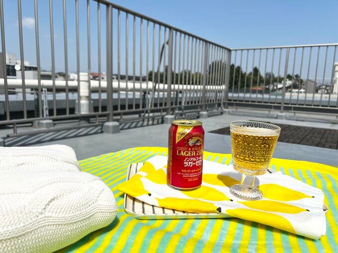 ベランダにレジャーシートを敷き、ノンアルコールビールとともに過ごすイメージ